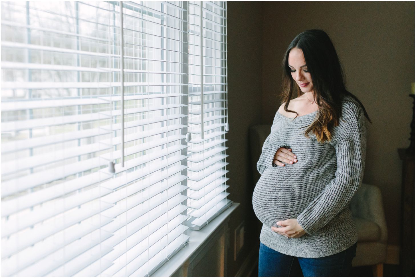mom poses near a window holding her pregnant belly