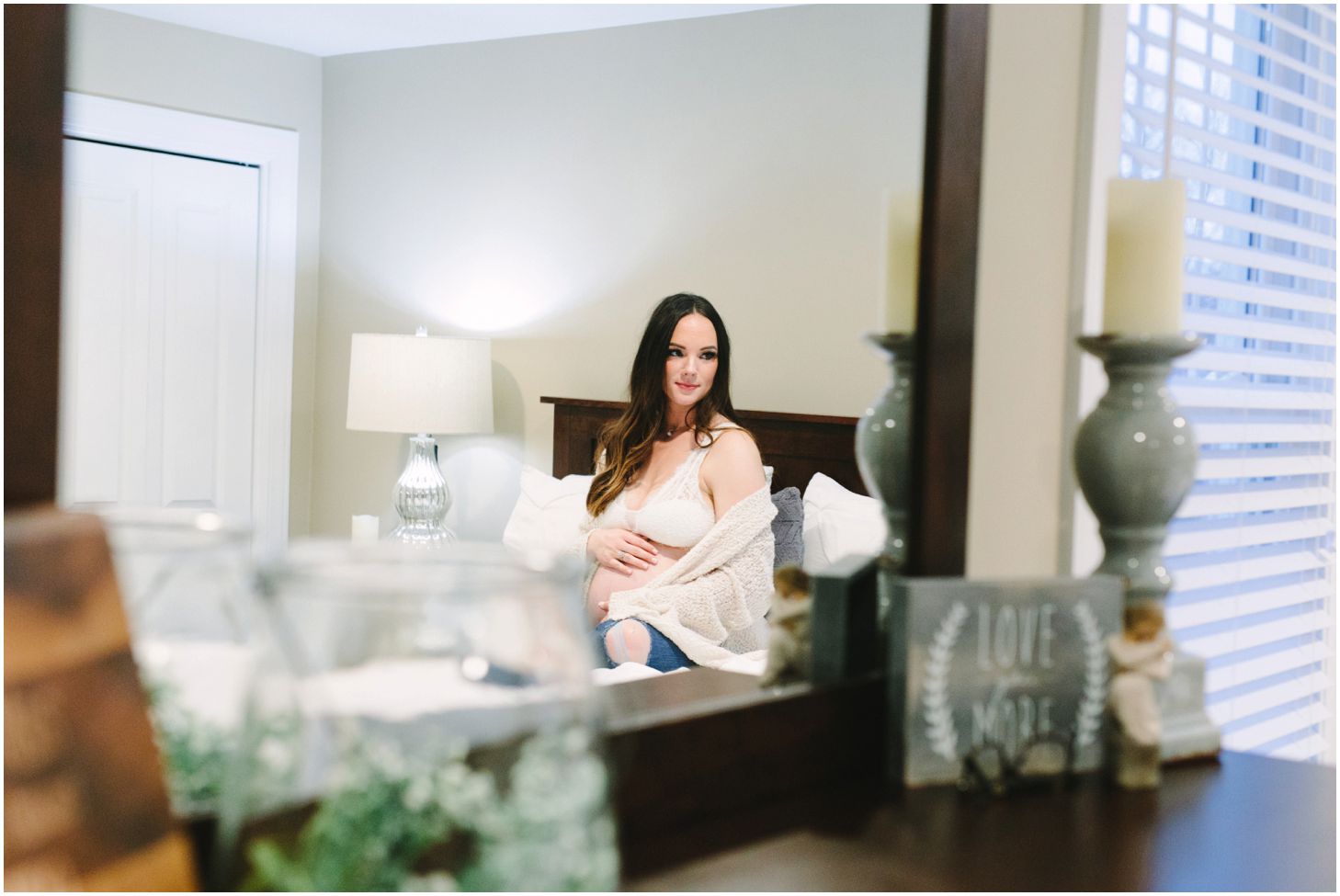 mirror reflection of mom holding her belly, sitting on a white bed | maternity session