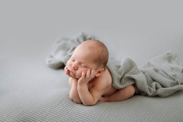 Side view of newborn baby with head in hands on a light gray background
