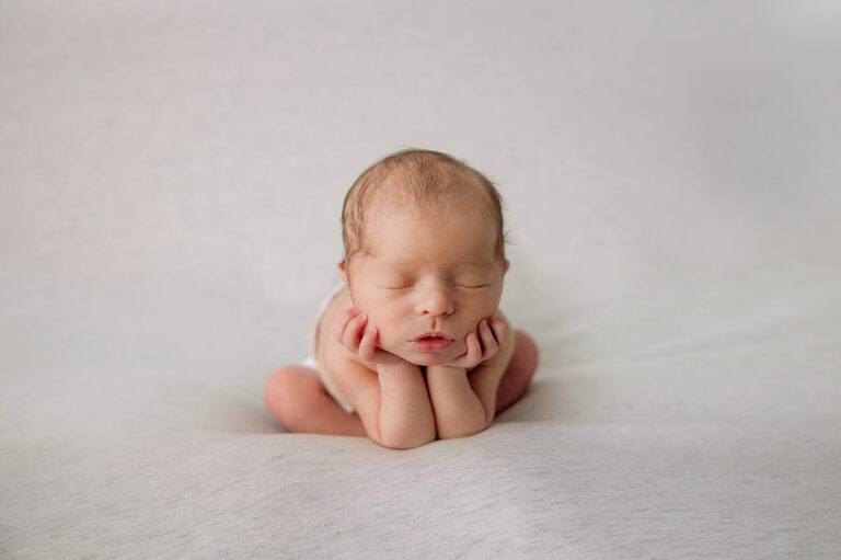 Newborn baby with head in hands on a cream background
