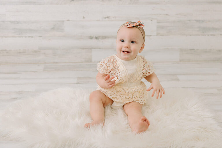 smiling six month old baby in ivory romper smiling with headband, sitter session