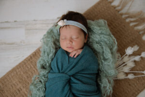 newborn baby girl wrapped in teal blanket in dough bowl