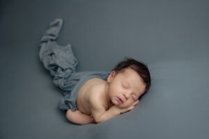 newborn baby boy sleeping on a gray/blue backdrop