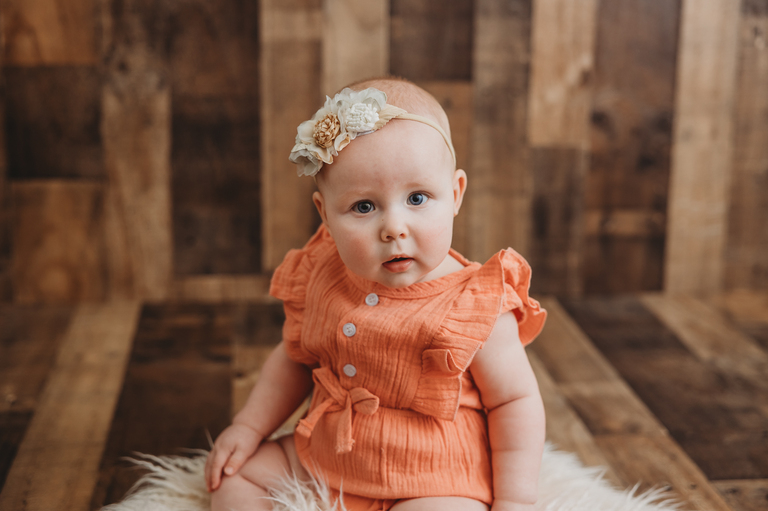 baby in orange outfit with headband, sitter session