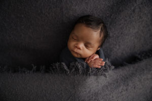 newborn sleeping baby tucked into a dark gray blanket