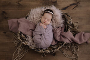 sleeping newborn baby girl wrapped in purple cloth lying in a basket