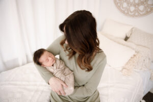 mom holding newborn baby boy with neutral blankets and backdrop