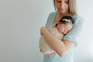 mom holding a newborn baby girl with a headband